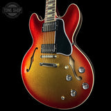 A close-up of an electric guitar body with a red-to-gold sunburst finish, black pickguard, chrome hardware, and f-holes, shown against a black background with a Tone Shop watermark in the top left.