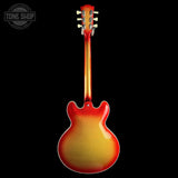 A classic electric guitar shown from the back, featuring a vibrant red and yellow sunburst finish against a solid black background. A Tone Shop logo is visible in the top-left corner.