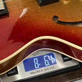 Close-up of a red glitter electric guitar body resting on a digital scale displaying 8.64 lbs.
