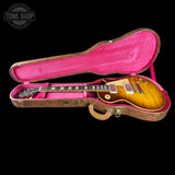A sunburst electric guitar resting inside an open hard case with a bright pink velvet interior, photographed against a solid black background. A Tone Shop watermark is visible in the top-left corner.
