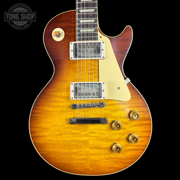 A classic electric guitar with a natural sunburst finish, featuring a cream pickguard, dual humbucker pickups, and gold-toned hardware, shown against a solid black background.