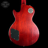 The back of a Gibson Les Paul Custom electric guitar with a glossy reddish-brown cherry finish, featuring a black pickguard and a silver 'Gibson Les Paul Custom' emblem on the upper right side, shown against a solid black background.