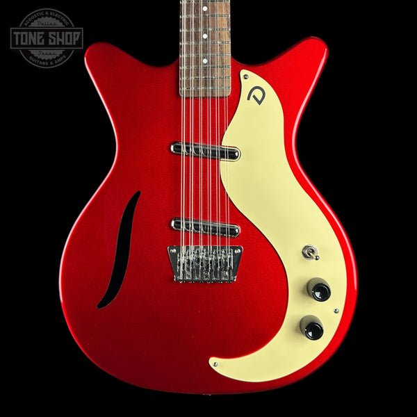 A red electric guitar with a cream-colored pickguard and maple top, shown against a solid black background. A Tone Shop watermark is visible in the upper left corner.