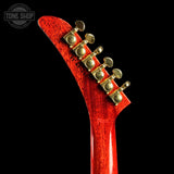 Close-up of the headstock of a guitar with a glossy red finish and gold tuning pegs, shown against a solid black background. A 'TONE SHOP' watermark is visible in the top-left corner.