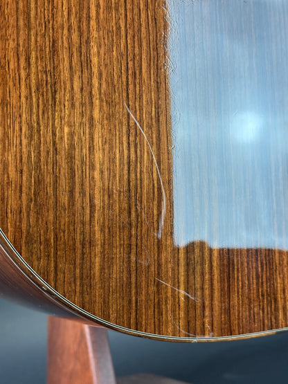 Close-up of a wooden guitar's soundboard with visible grain and a small scratch.
