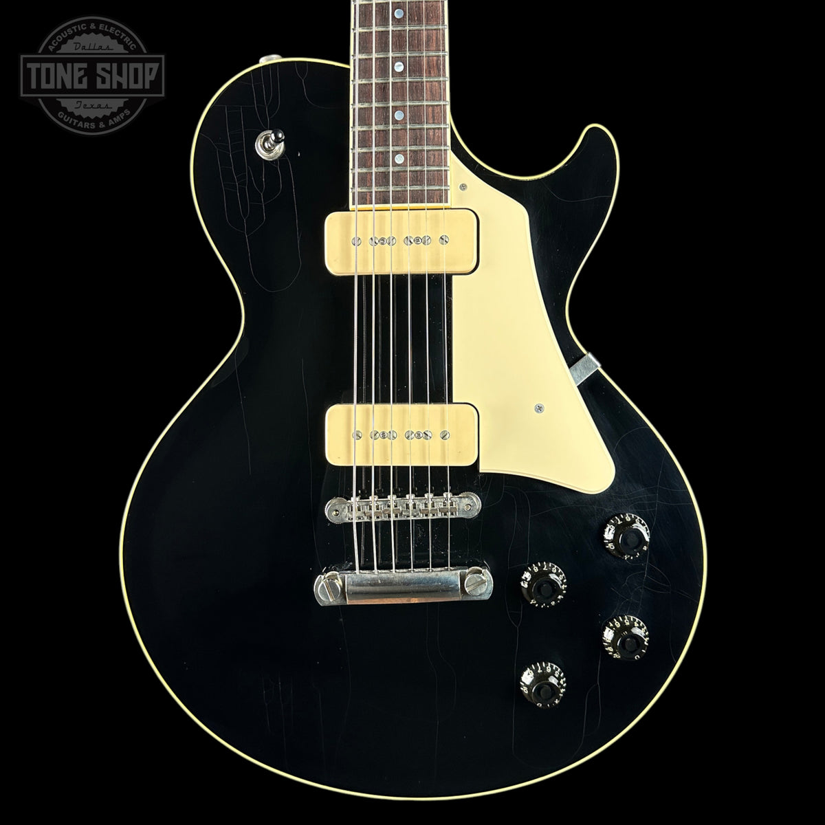 A black electric guitar with a cream pickguard and cream trim, featuring dual humbucker pickups and chrome hardware, shown against a solid black background with a Tone Shop logo in the top left corner.