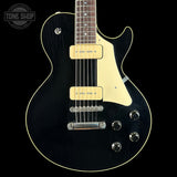 A black electric guitar with a cream pickguard and cream trim, featuring dual humbucker pickups and chrome hardware, shown against a solid black background with a Tone Shop logo in the top left corner.