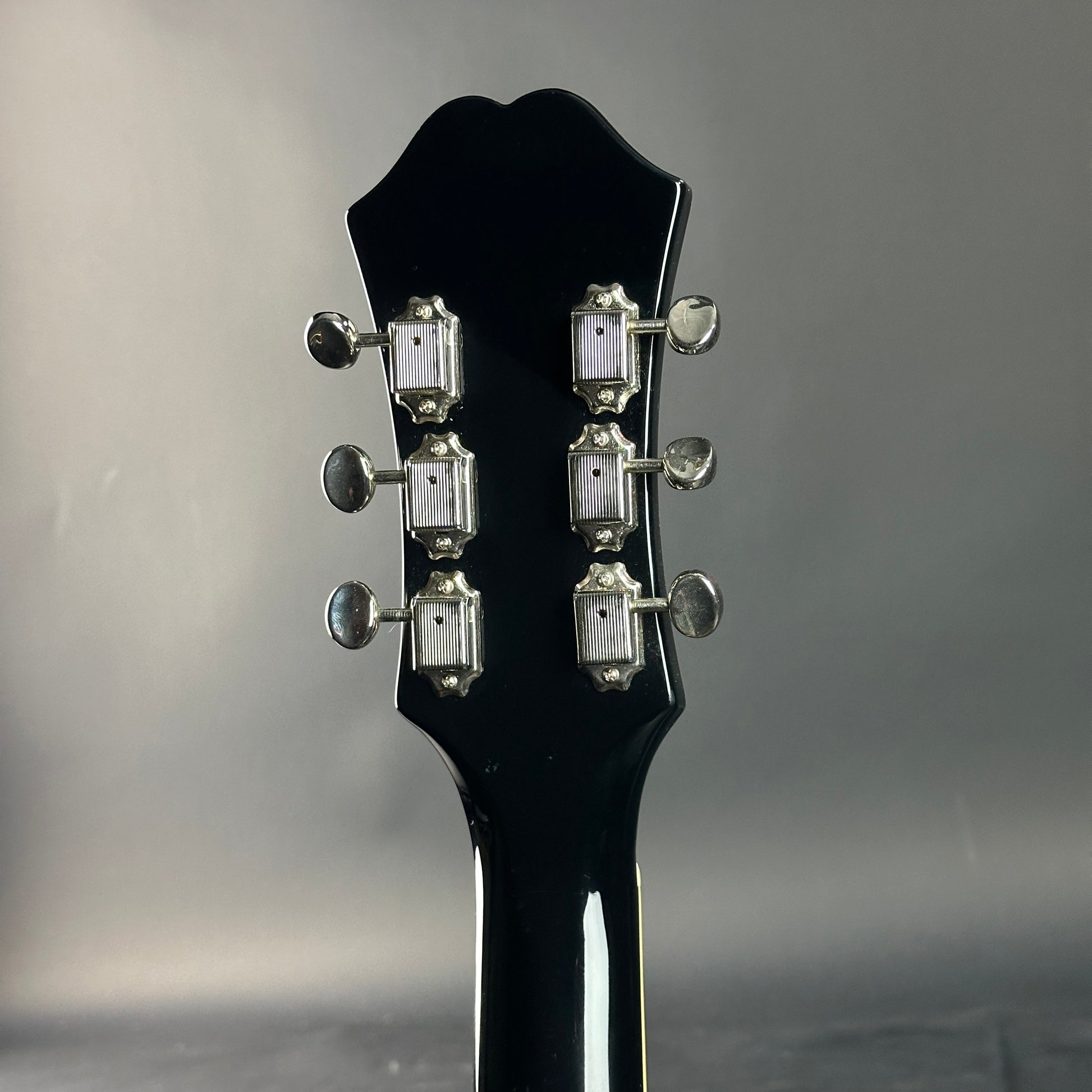 Close-up of a black guitar headstock with tuning pegs on a gray background