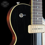 Close-up of a black electric guitar body with a gold edge, showing part of the neck, pickup, and control switch against a black background. A Tone Shop watermark is visible in the top left.