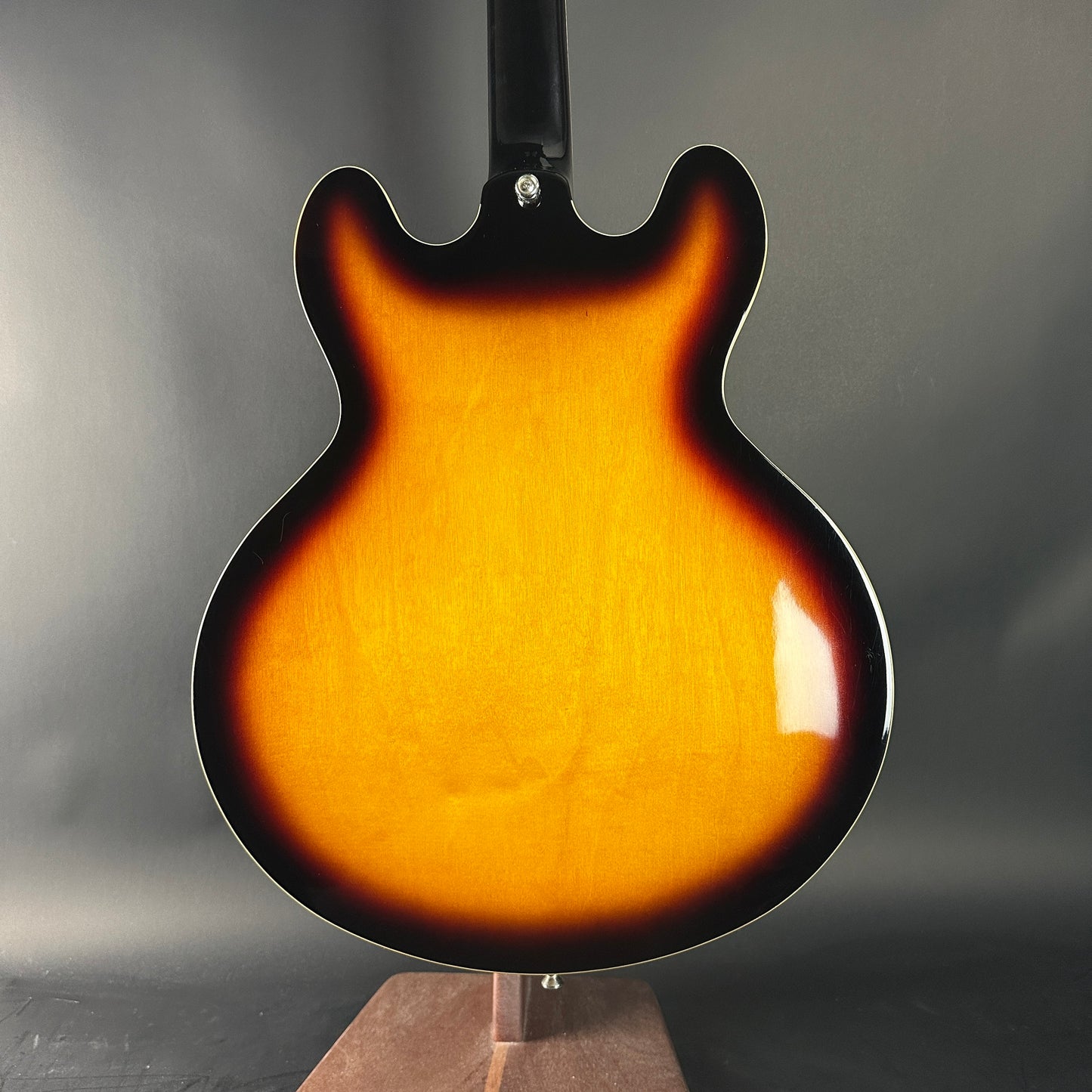 Glossy brown electric guitar body on a stand against a gray background