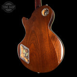 The back of a classic electric guitar with a glossy reddish-brown wood finish, featuring a chrome-covered volume pot and a chrome-covered pickup cover, set against a solid black background.