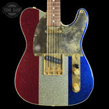 A custom electric guitar with a vertical tricolor glitter finish: red on the left, silver in the center, and blue on the right, with a distressed gold pickguard and gold-toned hardware. The neck is a dark wood fretboard.