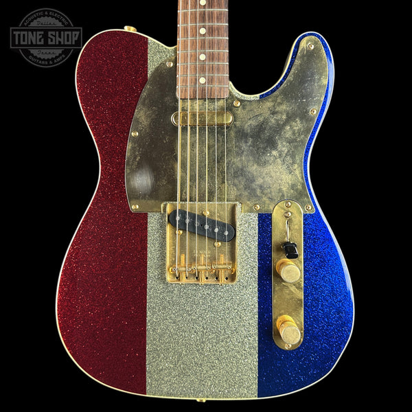 A custom electric guitar with a vertical tricolor glitter finish: red on the left, silver in the center, and blue on the right, with a distressed gold pickguard and gold-toned hardware. The neck is a dark wood fretboard.