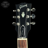 Close-up of a Gibson acoustic guitar headstock with six silver tuning pegs, white Gibson script logo, and a white crown emblem on a black background.