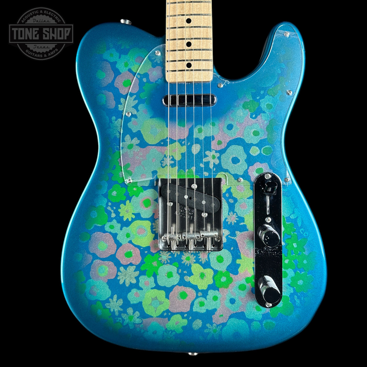 A blue electric guitar with a vibrant green, pink, and light blue retro floral pattern, shown against a solid black background with a Tone Shop watermark in the top-left corner.