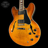A classic double-cutaway electric guitar with a vibrant orange sunburst finish, black pickguard, and chrome hardware, shown against a solid black background with a Tone Shop logo in the top-left corner.