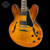 A classic double-cutaway electric guitar with a vibrant sunburst finish, featuring a black pickguard, chrome hardware, and a dark fretboard, shown against a solid black background with a Tone Shop watermark in the top left corner.