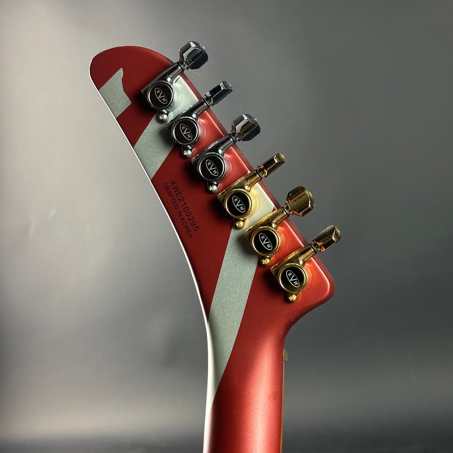 Close-up of a red electric guitar headstock with tuning pegs on a gray background