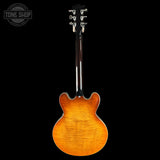 A classic double-cutaway electric guitar shown from the back, featuring a vibrant sunburst orange finish and a dark wood neck, set against a solid black background with a Tone Shop watermark in the top left corner.