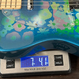 Close-up of a blue electric guitar with a colorful floral pattern on the body, resting on a digital scale displaying 7.41 lbs.