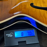 Close-up of a glossy sunburst electric guitar body resting on a black Smart Weigh digital scale displaying 8.7 kg.