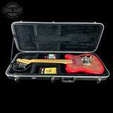An open black hard guitar case on a black background, containing a red electric guitar with gold floral inlay, a black coil, and small accessories. A Tone Shop watermark is visible in the top left corner.