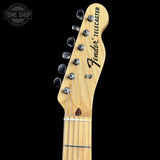 Close-up of a Fender Telecaster electric guitar headstock made of natural maple wood, featuring silver tuning pegs and a black Fender logo, set against a solid black background.