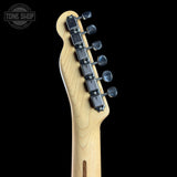 Close-up of the headstock of an electric guitar with a natural wood finish and six black tuning pegs, shown against a solid black background with a Tone Shop watermark in the top left corner.