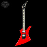 A bright red electric guitar with a distinctive angular body, black hardware, and a dark fretboard, shown against a solid black background. A Tone Shop watermark is visible in the top-left corner.