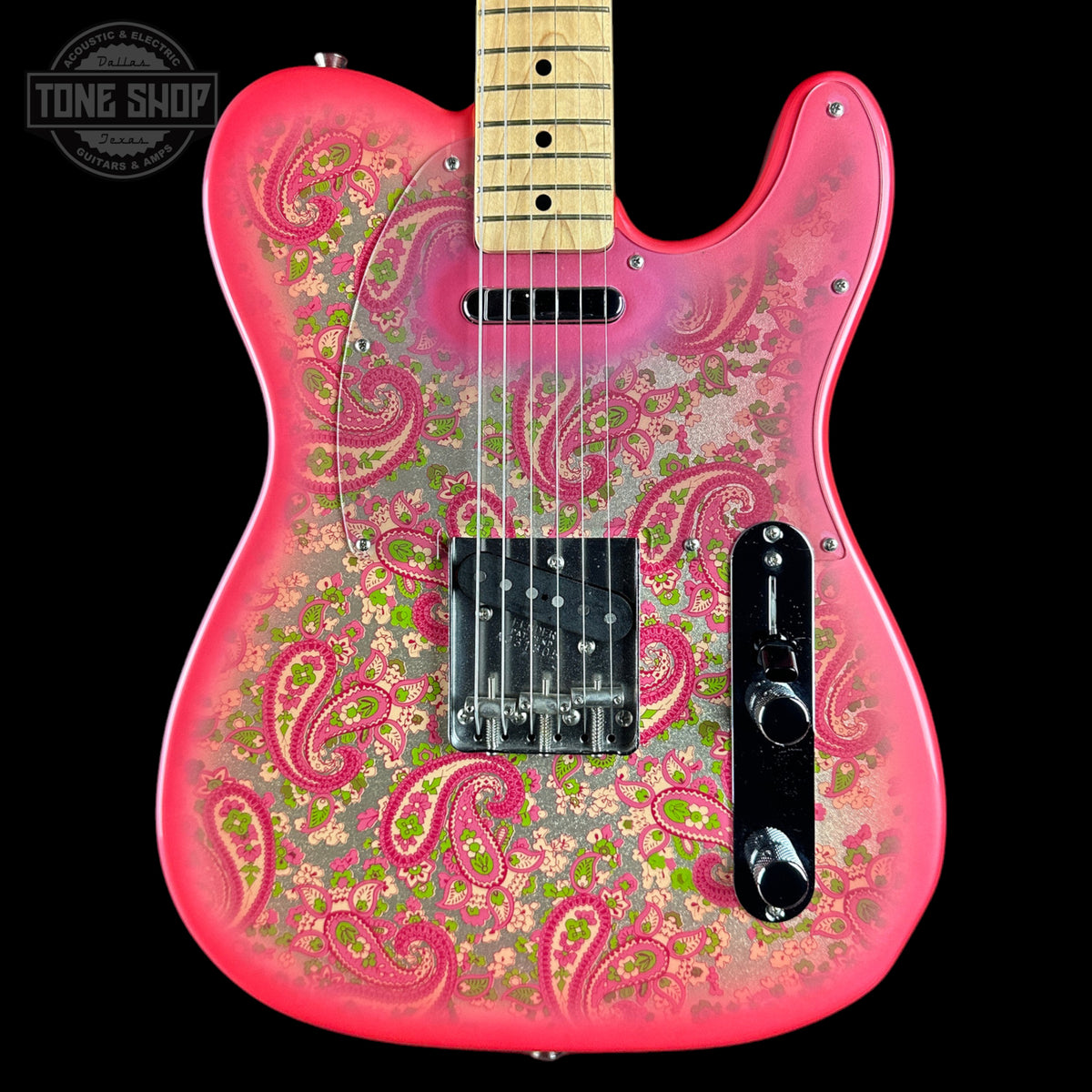 A pink electric guitar with a vibrant paisley and floral pattern in pink, green, and gold over a glossy finish, shown against a solid black background with a Tone Shop watermark in the top left corner.