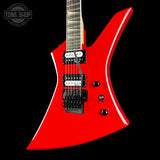 A bright red electric guitar with a distinctive angular body, black hardware, and a dark fretboard, shown against a solid black background. A 'TONE SHOP' watermark is visible in the top-left corner.