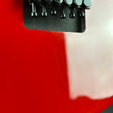 Close-up of a glossy red guitar body with a black bridge and tuning pegs visible at the top.