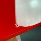 Close-up of a glossy red surface with a small clear liquid droplet and a scratch near the bottom edge, against a mostly out-of-focus dark background.