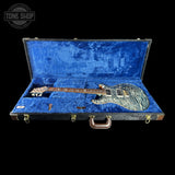 An electric guitar with a blue and gray marbled finish resting inside an open blue velvet-lined hard case, shown against a solid black background with a Tone Shop logo in the top-left corner.