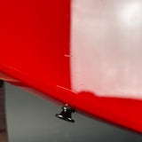 Close-up of a glossy red vehicle body panel with a small black metal fastener or latch near the bottom edge.