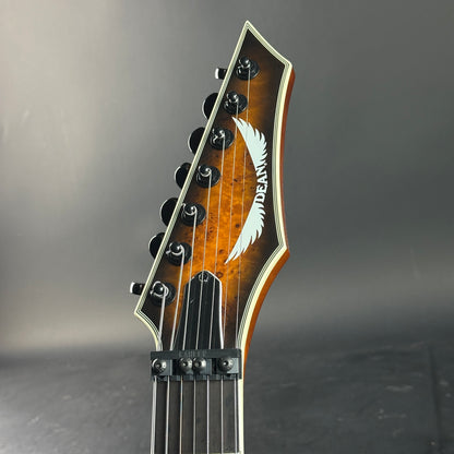 Close-up of a guitar headstock with a brand logo on a gray background