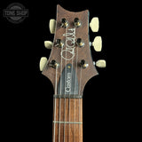 Close-up of a guitar headstock with a dark brown wood finish, cream tuning pegs, and a black pickguard with the word 'Custom' in white. A Tone Shop watermark is visible in the top left corner.
