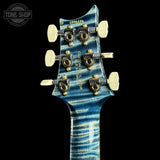 Close-up of a guitar headstock with a blue flamed maple finish, six gold-and-white tuning pegs, and visible model text reading 'CS 0396236' and 'CROWN SKINGS'.