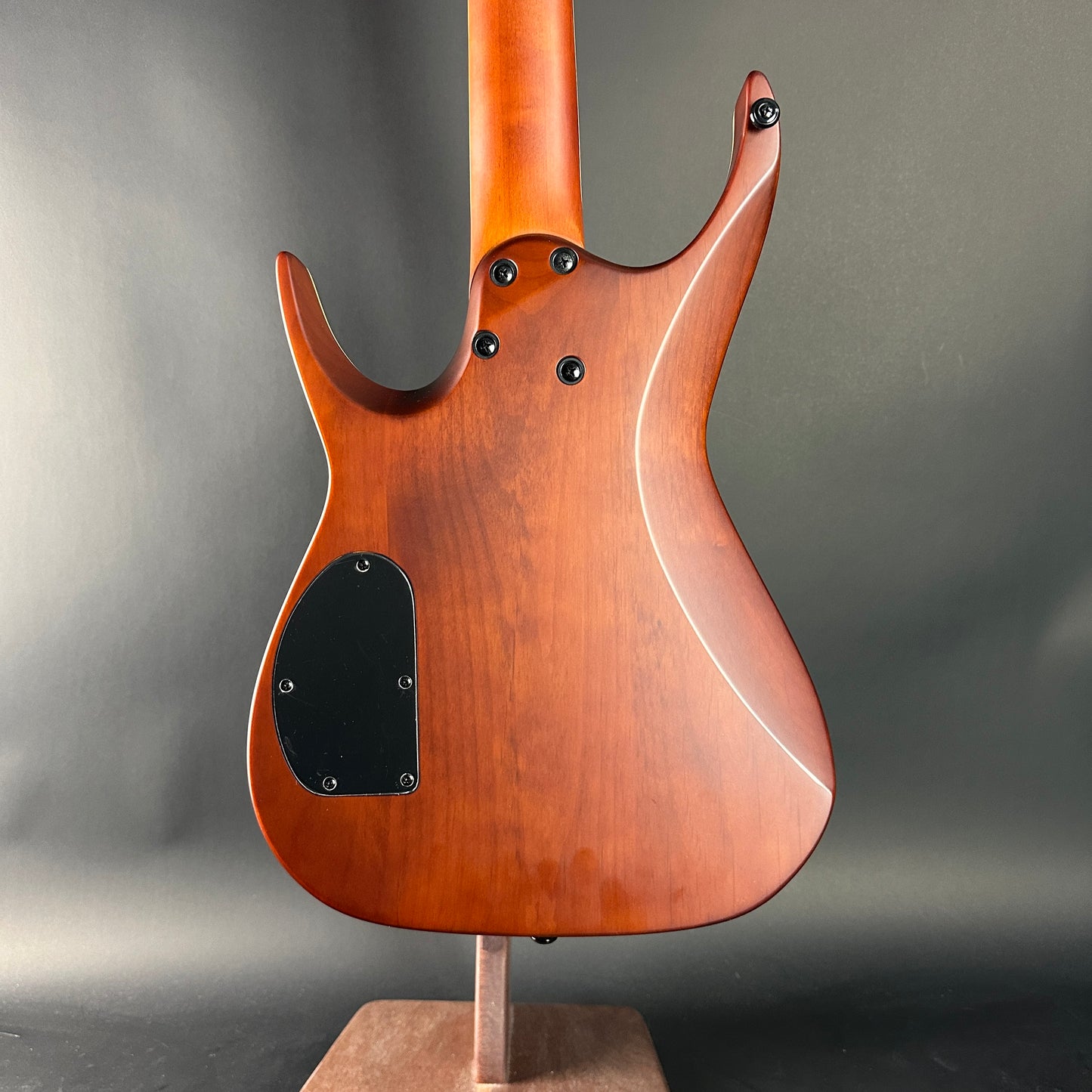 Wooden electric guitar body on a stand against a gray background