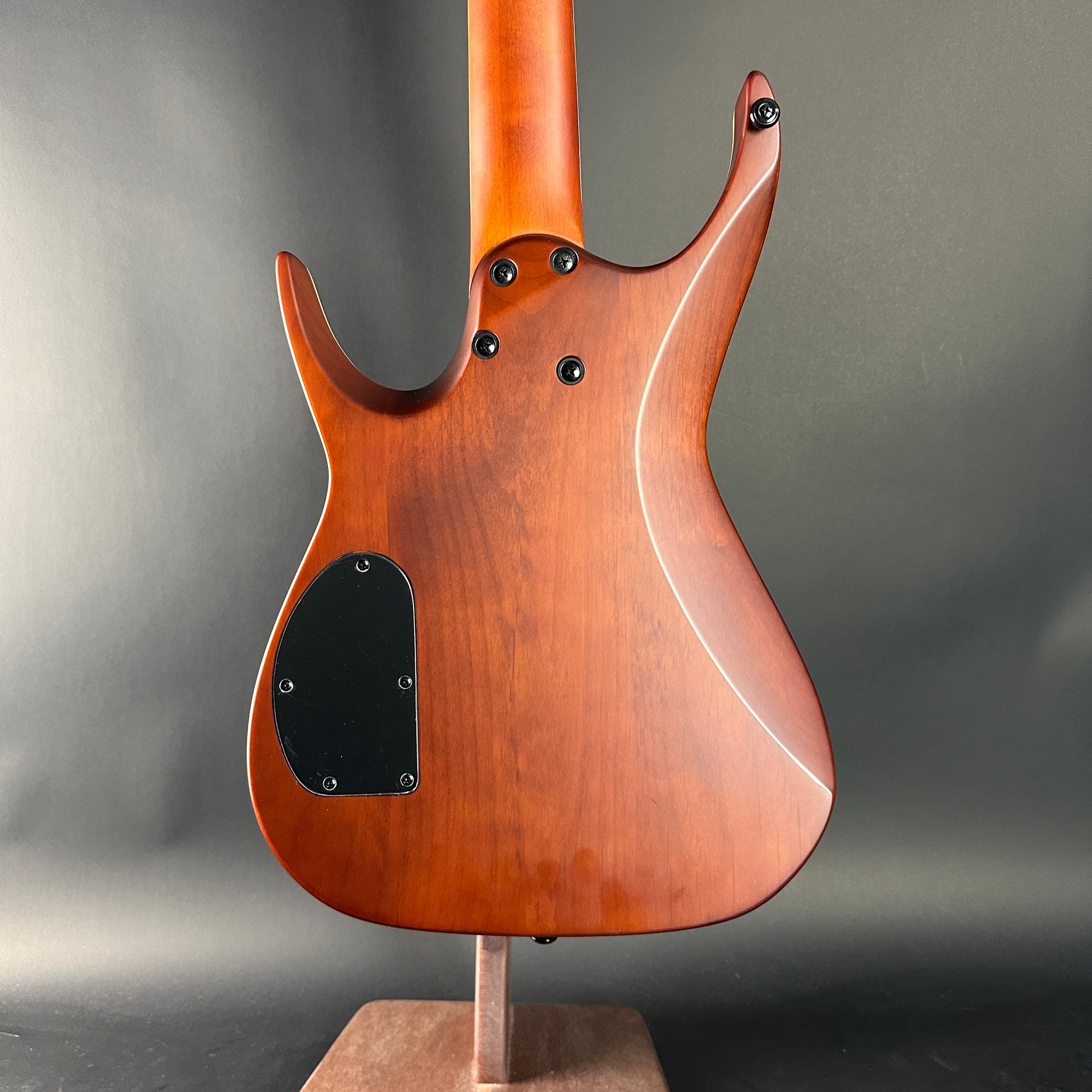 Wooden electric guitar body on a stand against a gray background