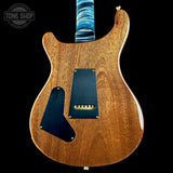 The back of an electric guitar with a natural wood body, blue pickguard, and blue neck, shown against a black background with a Tone Shop watermark in the top left corner.