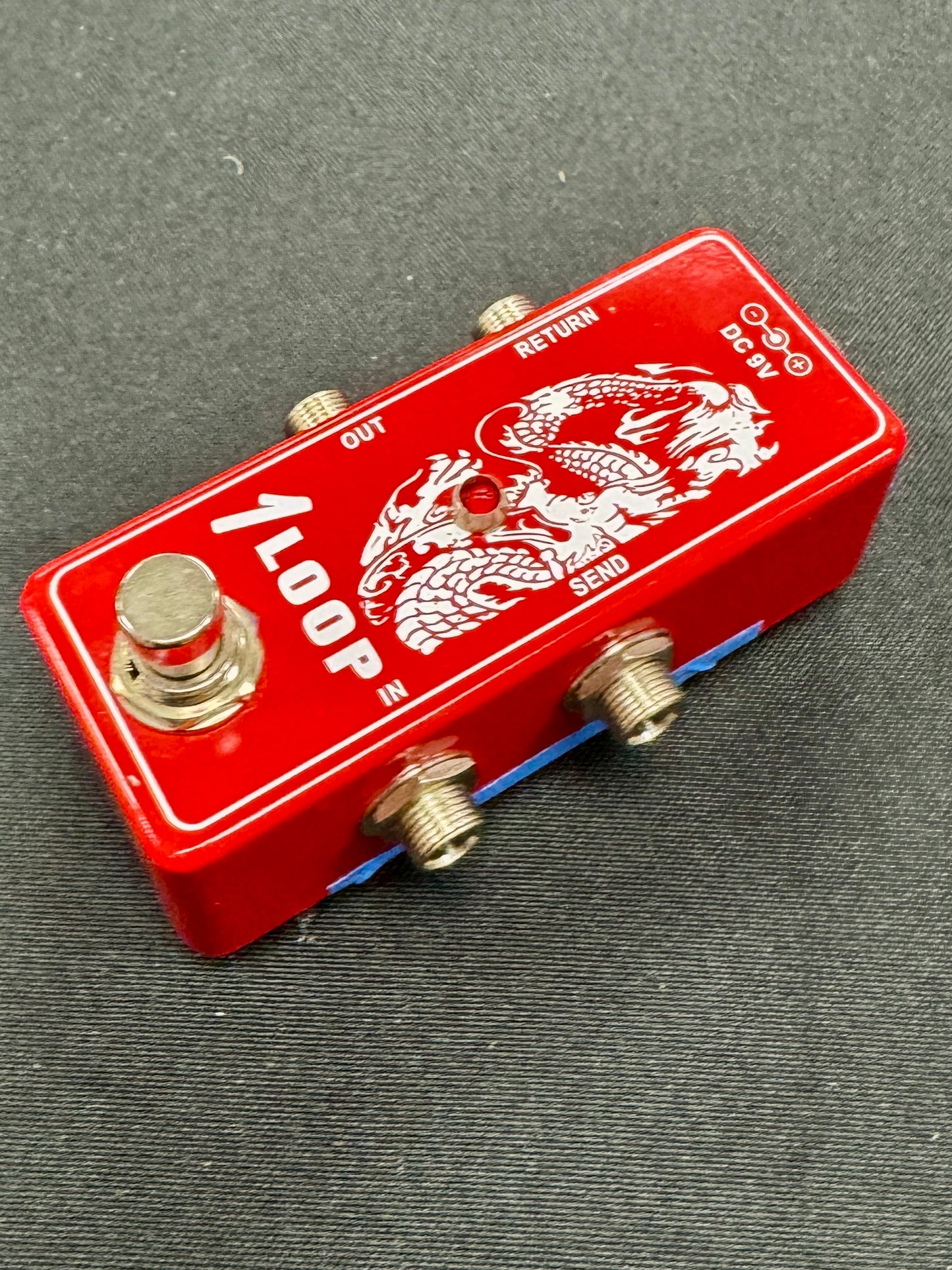 Red guitar effects pedal with dragon design on a gray surface