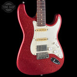 A red glitter electric guitar with a white pickguard and gold hardware, shown against a solid black background. A 'Tone Shop' logo watermark is visible in the top-left corner.