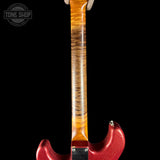 Close-up of the neck and lower body of an electric guitar against a black background, showing a flame maple wood neck with orange and brown grain and a metallic red body.