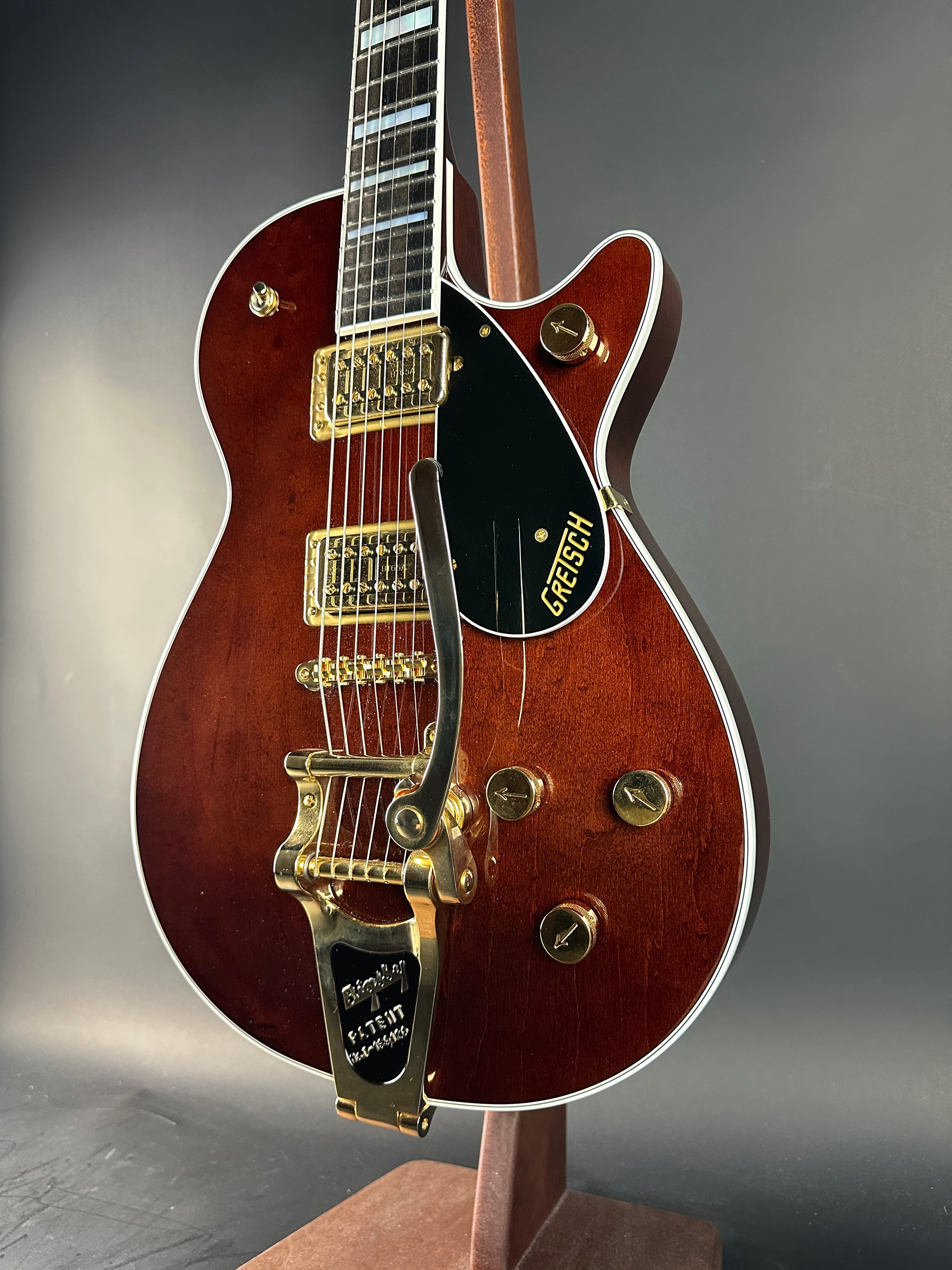 Close-up of a brown electric guitar with gold hardware on a gray background