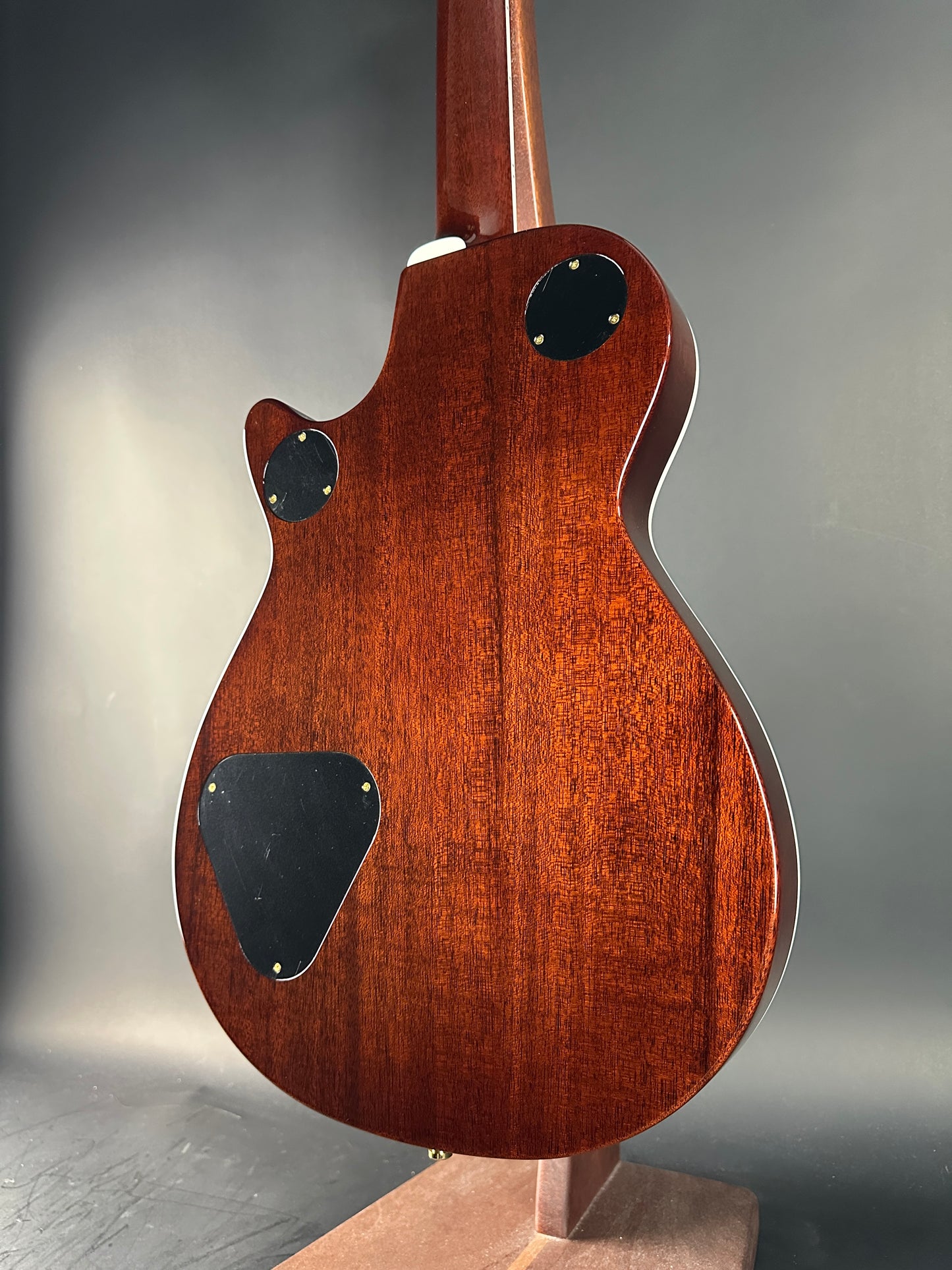 Close-up of a wooden electric guitar body with a dark finish on a gray background