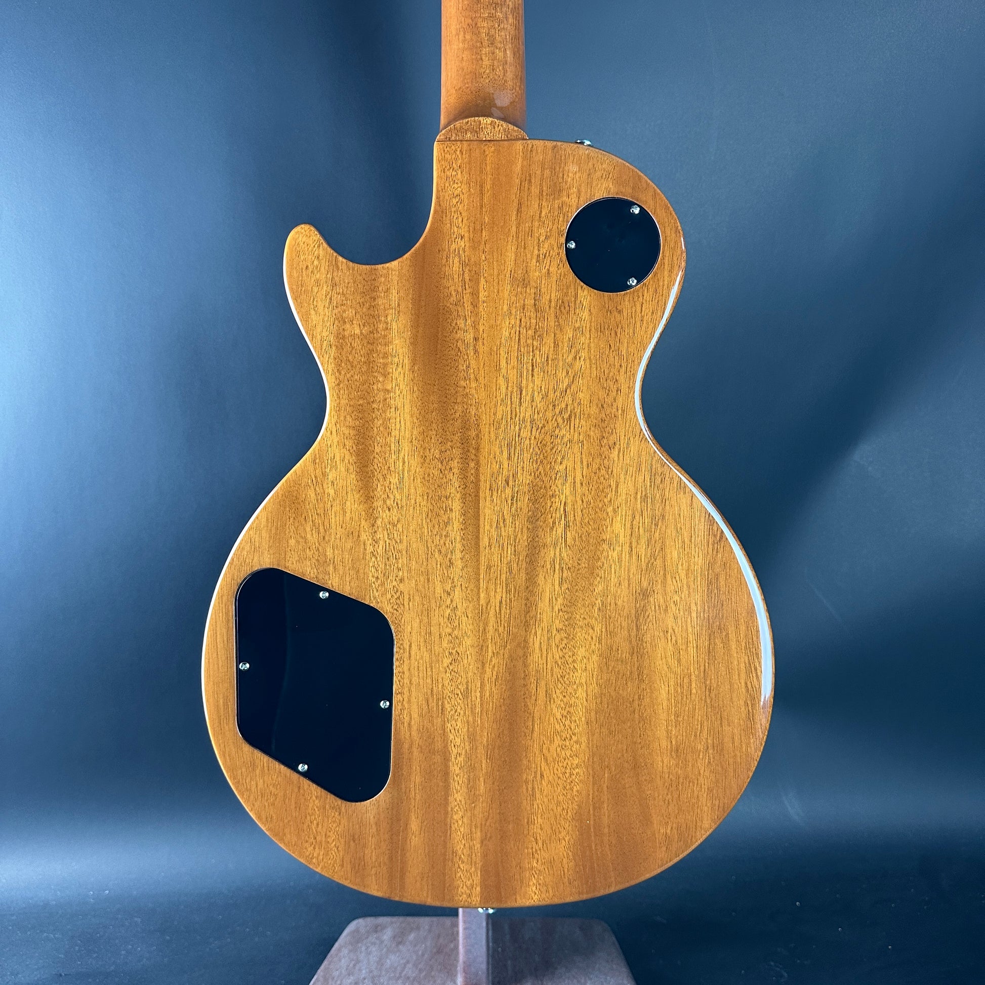 Wooden guitar body on a stand against a blue background
