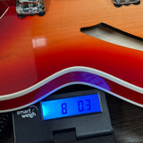 Close-up of a sunburst electric guitar body resting on a black Smart Weigh electronic scale displaying 8.03 kg.