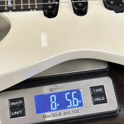 Digital scale displaying weight of a white object, with a guitar in the background.