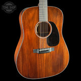 A close-up studio shot of an acoustic guitar body made from rich, warm brown wood with a glossy finish, featuring a black pickguard and silver-toned hardware, set against a solid black background.